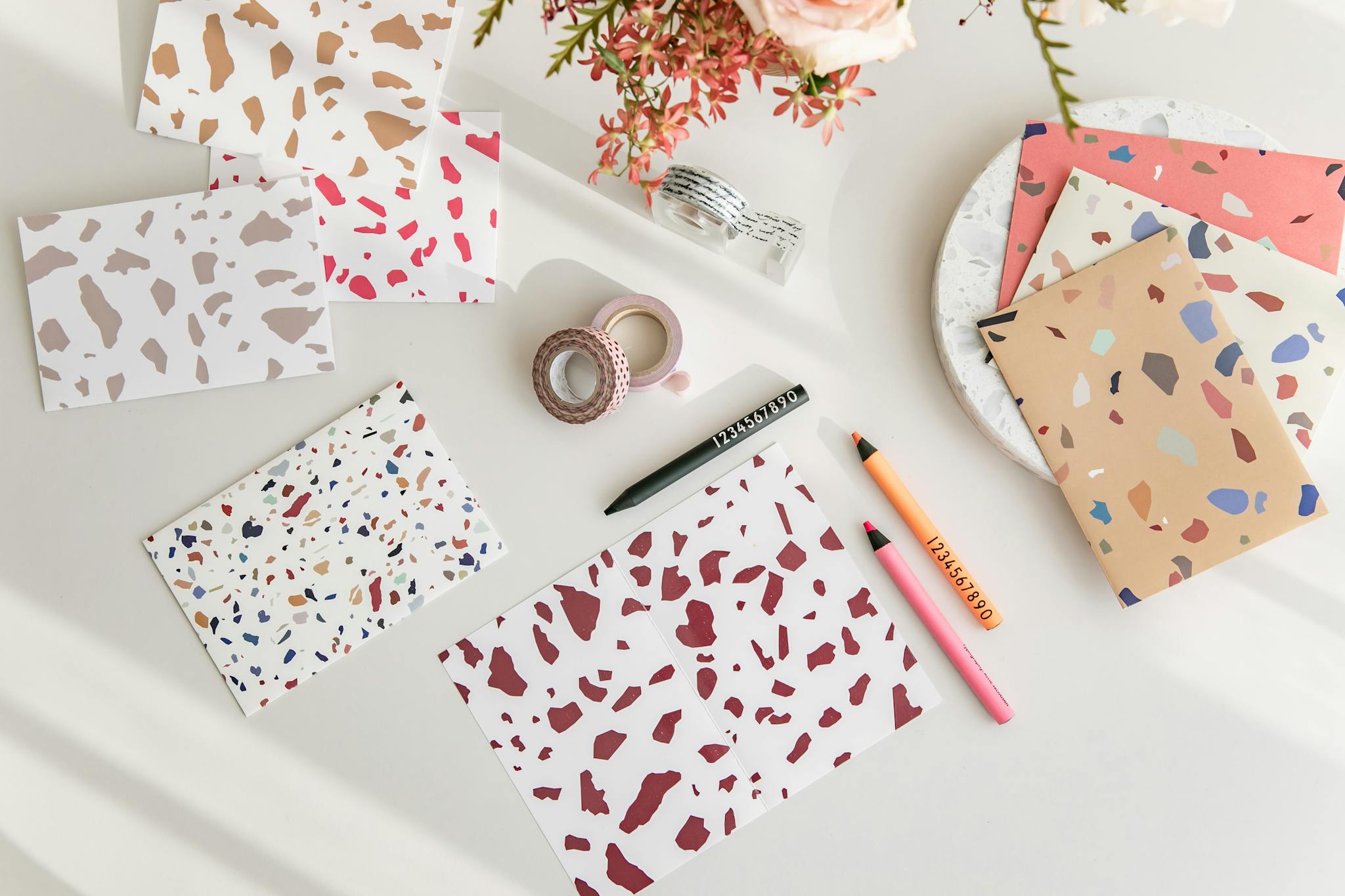 Terrazzo pattern stationery and pink flowers on a white table, perfect for modern and artistic themes.